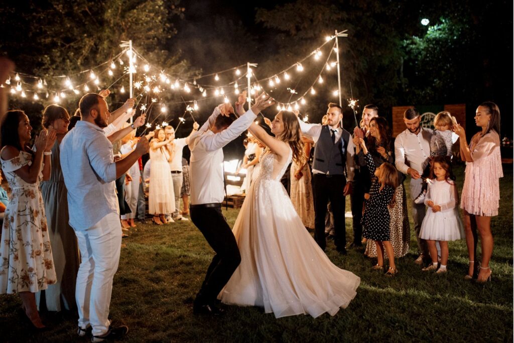 Bride and groom dancing at an outdoor evening wedding reception with string lights and sparklers, featuring professional DJ entertainment.