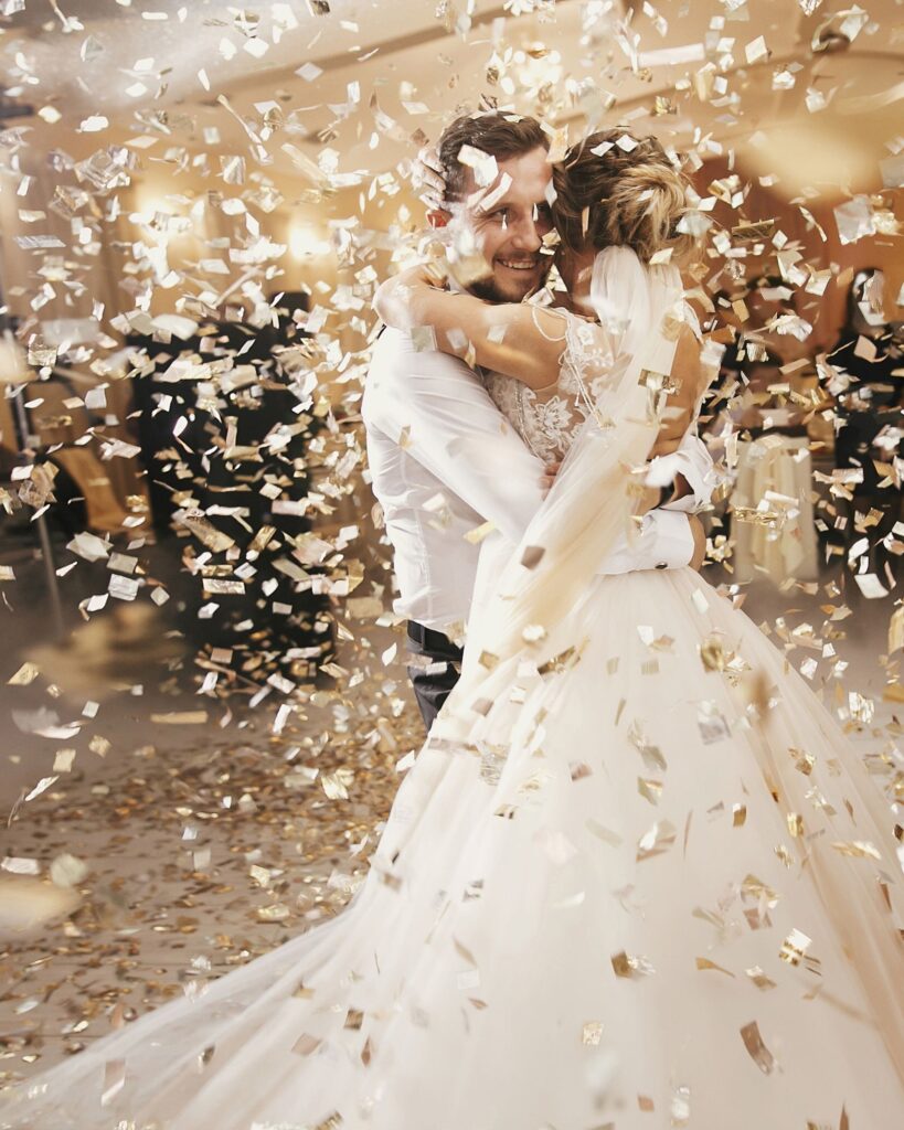 A bride and groom embracing on the dance floor during a gold confetti blast, highlighting professional wedding DJ special effects and entertainment.